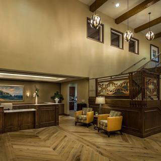 A warmly lit hotel lobby featuring a reception desk, comfortable seating, and elegant chandeliers.