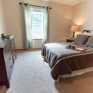 A cozy bedroom with a neatly made bed, a lamp on the nightstand, and a dresser near the window.