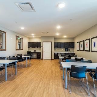 A modern classroom setup with tables and chairs on a wooden floor, well-lit and featuring wall decorations.