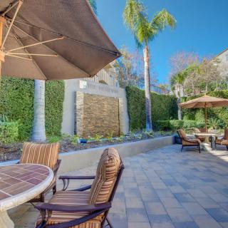 A sunny patio with outdoor furniture and umbrellas, surrounded by lush plants and palm trees.