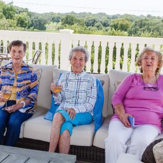 Three women enjoying a sunny day on a patio, sharing drinks and conversation.
