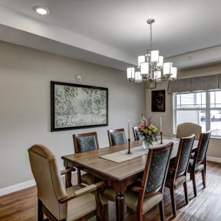 A modern dining room featuring a large wooden table surrounded by chairs, illuminated by a stylish chandelier overhead.