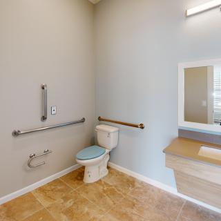 An accessible bathroom with grab bars and a mirror above the sink.
