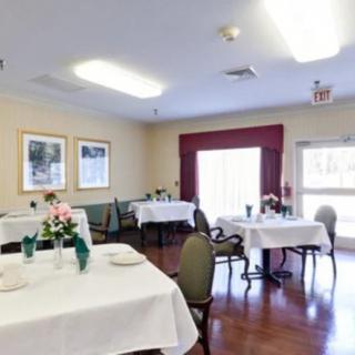 A cozy dining area with neatly arranged tables and chairs, decorated with flowers and lit by soft overhead lights.