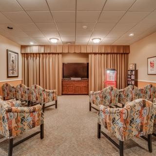 A cozy waiting room with floral chairs arranged around a television, featuring warm lighting and neutral tones.