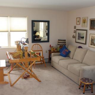 A cozy living room featuring a beige sofa, a weaving loom, and various pieces of wall art.