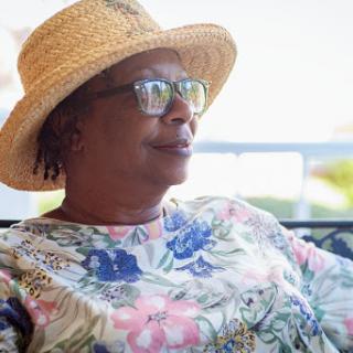 A woman enjoying a sunny day outdoors, wearing a floral shirt and a straw hat.