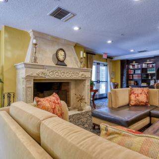 A cozy living room with a fireplace and comfortable seating area, featuring warm tones and a small library.