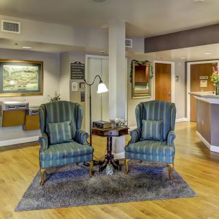 A cozy lobby area featuring two striped armchairs, a small table with a lamp, and wall artwork.