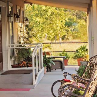 A cozy porch featuring a rocking chair and a child's bicycle, surrounded by greenery on a sunny day.