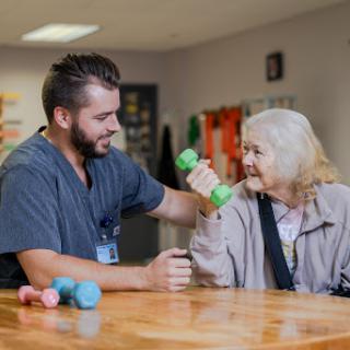 A caregiver assisting an elderly woman with her exercise routine using a dumbbell.