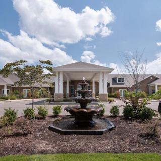 An elegant building with a landscaped entrance and a central fountain under a blue sky.