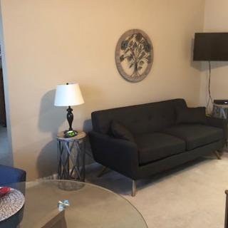 A cozy living room featuring a dark sofa, lamp, side tables, and decorative wall art.