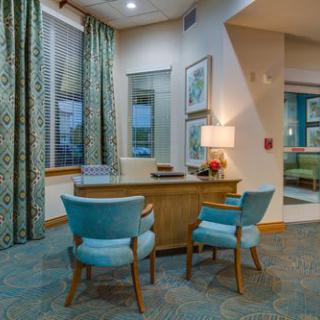 A modern office interior with a wooden desk, two turquoise chairs, and decorative elements like a lamp and artwork.