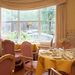 A cozy dining room with elegantly set tables near a large window offering a garden view.