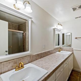A spacious bathroom with double sinks, mirrors, and a tiled countertop.