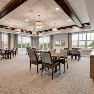 A modern dining room interior featuring tables and chairs, with ample natural light from large windows.