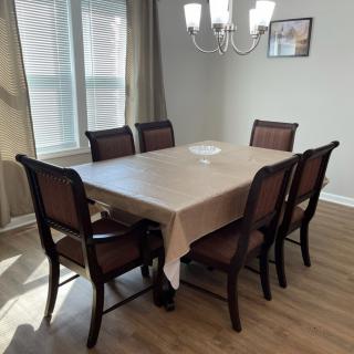 A dining room with a rectangular table and six chairs, illuminated by a chandelier.