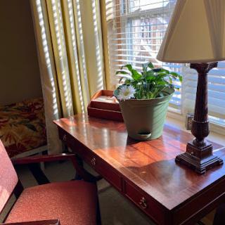 A cozy workspace featuring a wooden desk, a comfortable chair, and a potted plant, illuminated by sunlight streaming through the window.