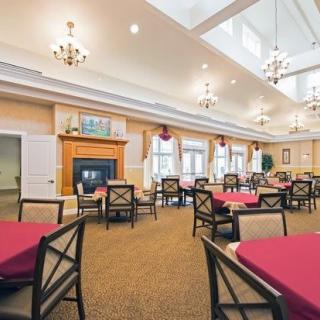 A spacious dining room with neatly arranged tables and chairs, featuring a fireplace and chandeliers under a bright ceiling.