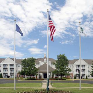 A building with flags in front, surrounded by well-maintained greenery and a partly cloudy sky.