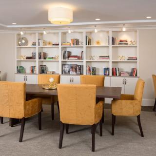A modern dining room featuring a large table surrounded by orange upholstered chairs, set against a backdrop of well-organized bookshelves.