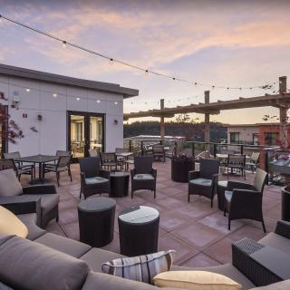 A stylish rooftop terrace with cozy outdoor seating and string lights, set against a beautiful sunset sky.