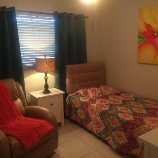 A cozy bedroom with a single bed, upholstered chair, and bedside lamp.