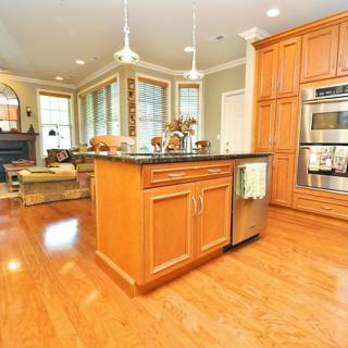 A modern kitchen with wooden cabinets, a central island, and hardwood flooring.