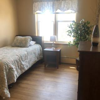A cozy bedroom featuring a single bed, a nightstand with a lamp, and natural light from the window.