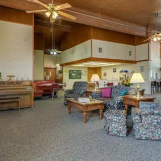 A spacious living room with various seating areas, a piano, and ceiling fans.
