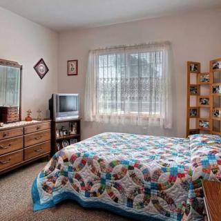 A cozy bedroom with a quilted bedspread, wooden dresser, and TV by the window.