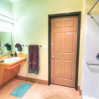 A modern bathroom featuring a large mirror, sink, and a shower with a wooden door.