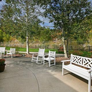 A serene outdoor garden area featuring white benches and chairs along a curved pathway surrounded by lush trees.