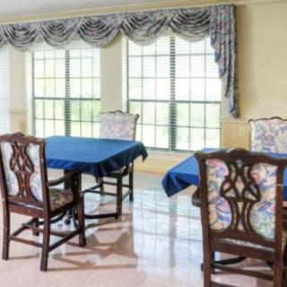 A dining room with blue tablecloths, ornate chairs, and large windows with draped curtains.