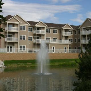 A residential apartment building with a pond and fountain in the foreground.
