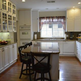 A spacious kitchen with an island and seating, featuring white cabinets and hardwood floors.