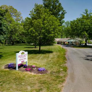 A scenic view of a tree-lined road with colorful flowers and a welcoming sign.