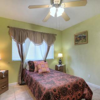 A cozy bedroom with a single bed featuring patterned bedding, flanked by nightstands with lamps, and a ceiling fan overhead.