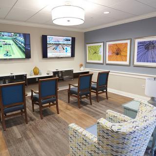 A modern conference room with chairs, tables, wall-mounted TV screens, and colorful artwork.