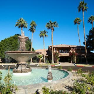 A scenic view of a resort featuring a fountain surrounded by palm trees under a clear blue sky.
