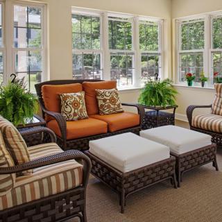 A cozy sunroom with wicker furniture and vibrant cushions, surrounded by large windows allowing natural light in.