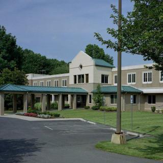 A modern hospital building surrounded by greenery and a driveway leading to the entrance.