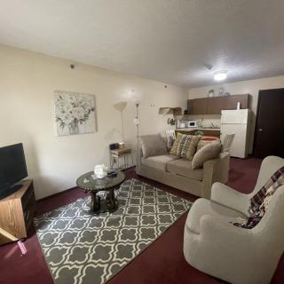 A cozy living room with a sofa, coffee table, and television, adjacent to a small kitchen area.