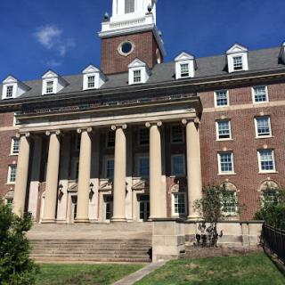 A grand brick building featuring impressive columns and a clock tower, set against a clear blue sky.