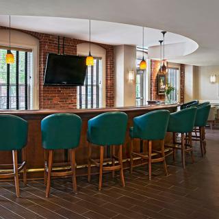 A modern bar interior with teal chairs, a wooden counter, and a wall-mounted TV.