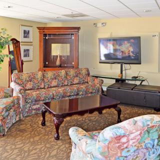 A cozy living room with floral-patterned sofas, a wooden coffee table, and a television mounted on the wall.