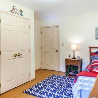 A cozy bedroom featuring a neatly made bed, a patterned rug, and a bedside table with a lamp.