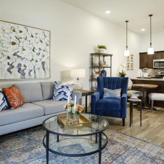 A contemporary living room with modern decor, featuring a cozy sofa, armchair, and stylish coffee table. The open layout extends to a dining area with pendant lighting.