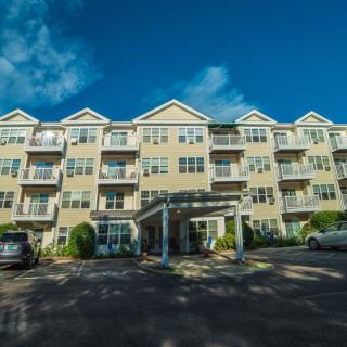 A four-story apartment building with a parking lot in front on a sunny day.